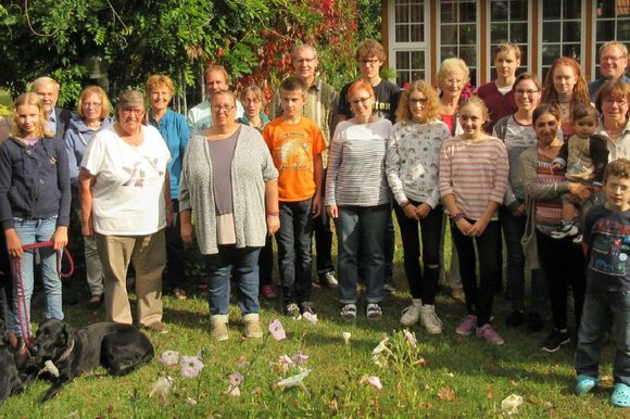 Eine große Gruppe Menschen aller Altersstufen stehen im Halbkreis. Hunde liegen davor.