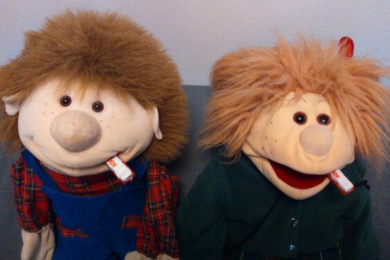 Die Handpuppen Lotti und Willi sitzen nebeneinander und haben einen Schokoriegel im Mund - Copyright: Ev.-Luth. Kirchengemeinde Schwarzenbek