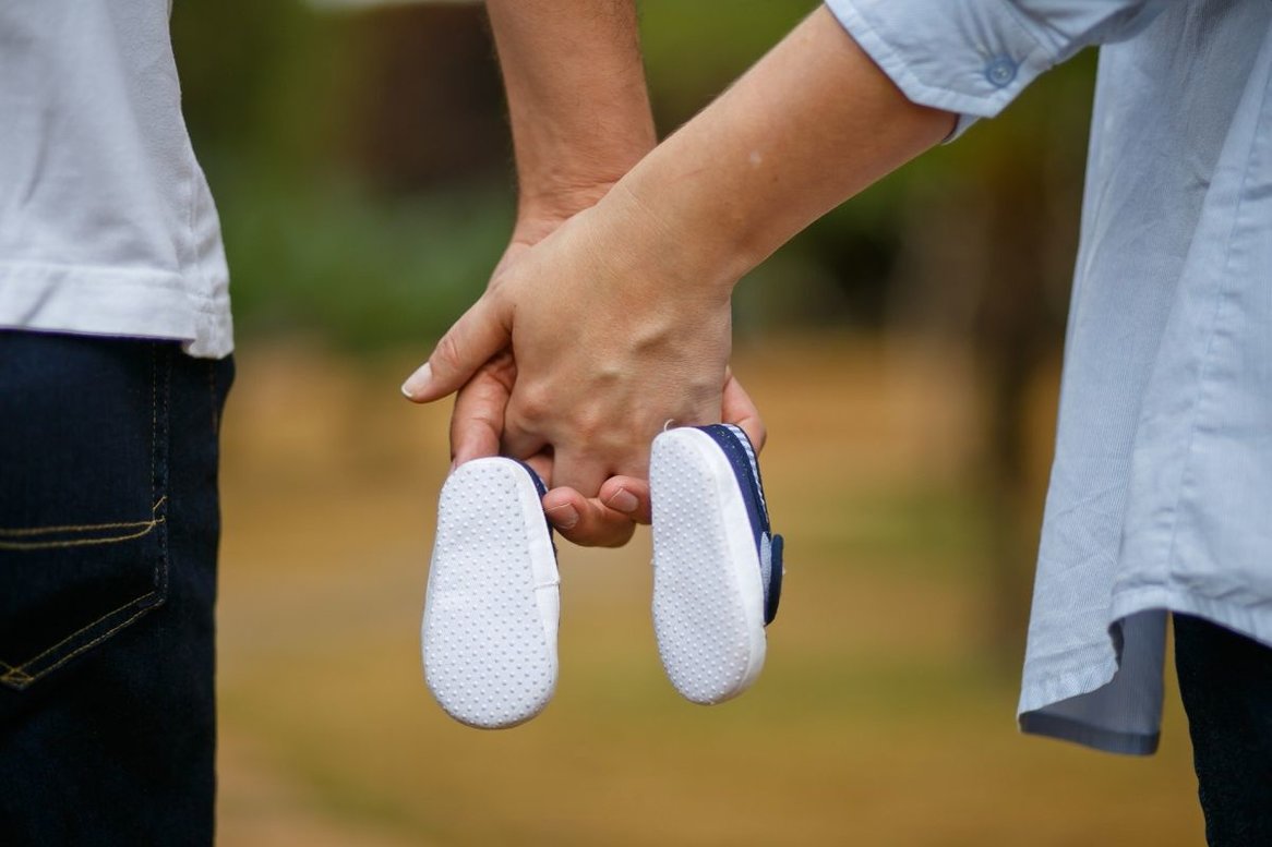 Hände von Mann und Frau die Babyschuhe in der Mitte halten