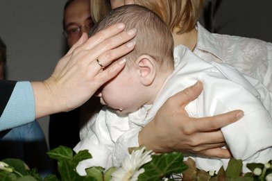 Kleines Kind wird über ein Taufbecken gehalten und es wird vom Pfarrer die Hand aufgelegt. - Copyright: pixabay baptism-331581_1920