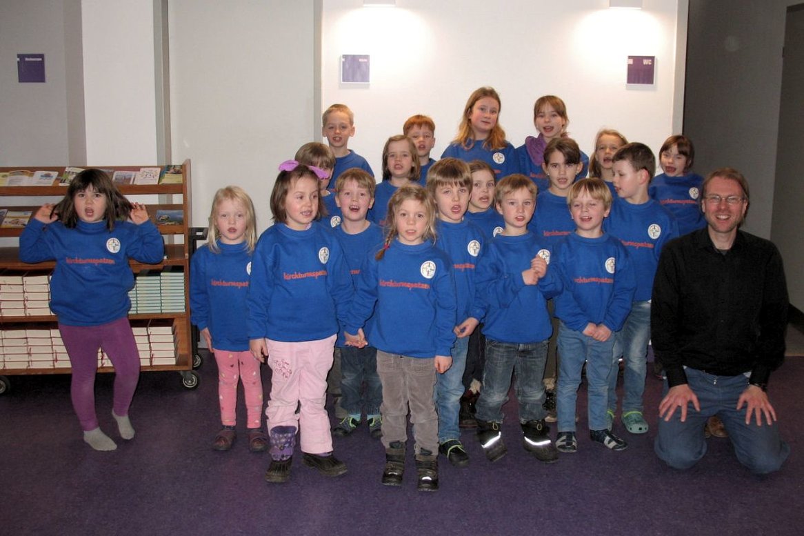 Kindergartenkinder alle in blauen Pullovern und ein knieender Chorleiter