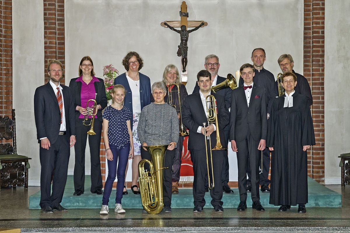 Erwachsene und Jugendliche mit Blechblasinstrumenten mit einer Pastorin in der Kirche