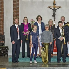 Erwachsene und Jugendliche mit Blechblasinstrumenten mit einer Pastorin in der Kirche
